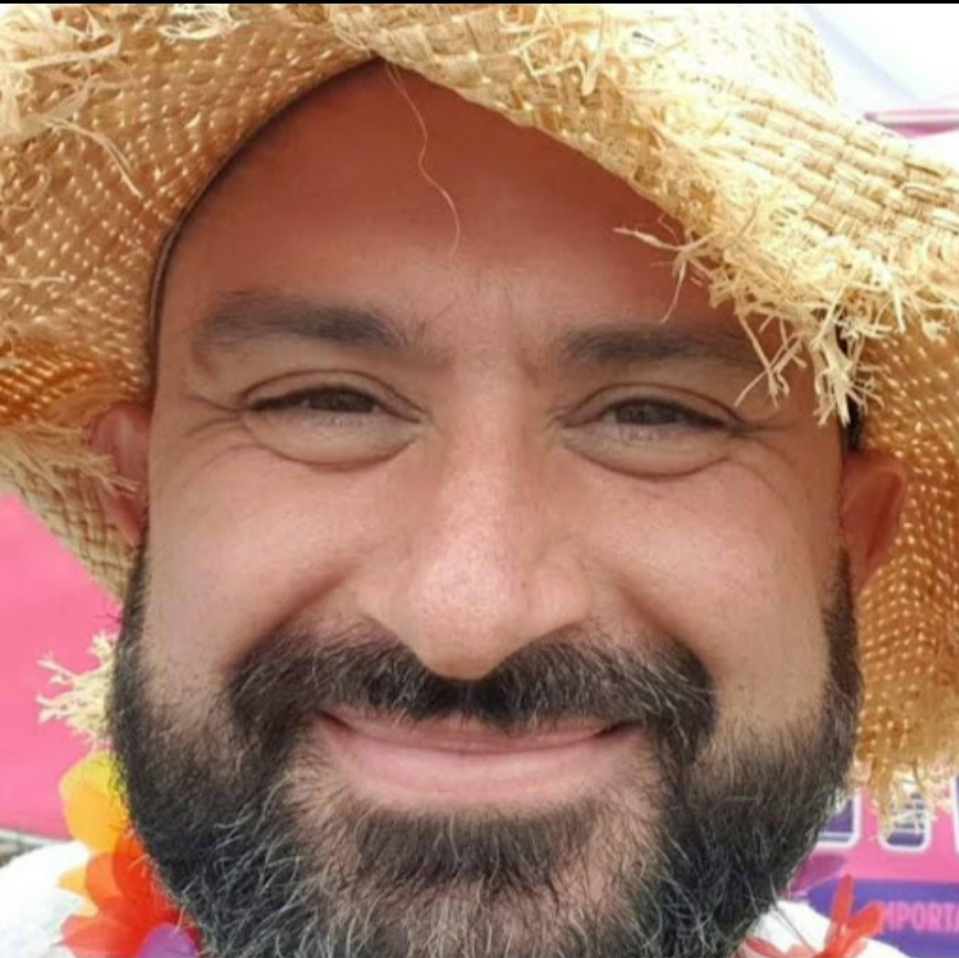 Chris, smiling, wearing a straw hat and a flower lei